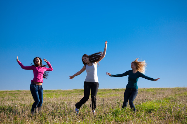 Three young beautiful woman jumping into the field against the s - 写真・画像