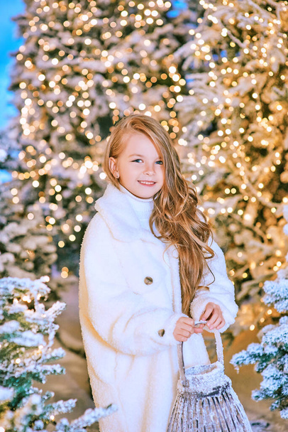 冬のクリスマスの森をライトで歩く白いエコファーコートのかわいい白人ブロンドの女の子。お正月童話のコンセプト - 写真・画像