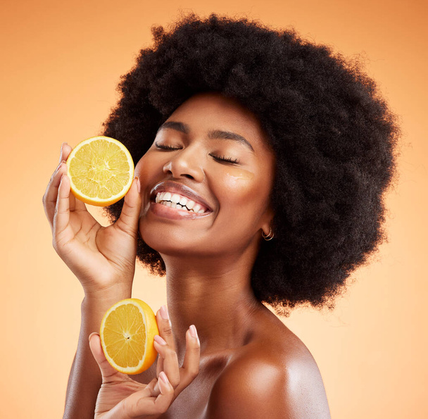 Beauty, skincare and orange with a model black woman in studio on a color wall background. Skin, health and vitamin c with a young female holding fruit for wellness, nutrition or natural treatment. - Foto, afbeelding