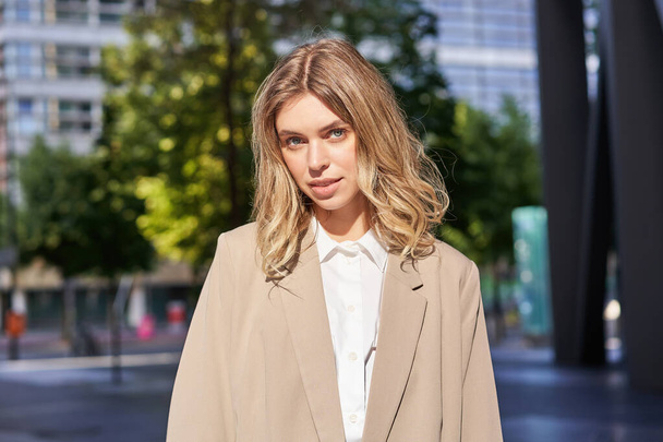Close up portrait of confident business woman, corporate lady in beige suit, looking determined and ready, standing outside office building on street. - Foto, afbeelding