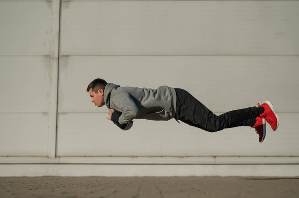 A man in a hoodie jumps while doing push-ups outdoors - Fotó, kép