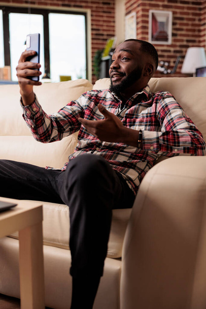 Άνδρας ελεύθερος επαγγελματίας που μιλάει στο online videoconference, χρησιμοποιώντας smartphone και webcam για να συνομιλήσει με συναδέλφους σε videocall συνάντηση. Εργασία εξ αποστάσεως από το σπίτι και να μιλάμε για το κινητό τηλέφωνο app. - Φωτογραφία, εικόνα