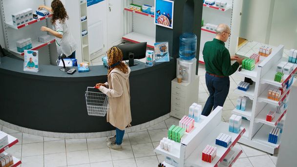 African american client buying pharmaceutical products and medicaments at drugstore counter, talking to pharmacist about medicine and drugs. Woman paying for supplements at pharmacy. - Valokuva, kuva