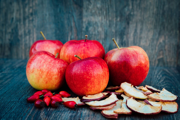 Jablka, sušená jablka a růžové boky leží na tmavém dřevěném stole Podzim. Kvalitní fotografie - Fotografie, Obrázek