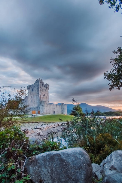 Antigua fortaleza antigua ruina del castillo de Ross con un lago, hierba verde y nubes de color naranja. Parque Nacional de Killarney, co Kerry, Irlanda. Foto de alta calidad - Foto, Imagen
