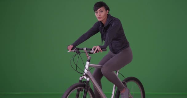 Millennial femme noire sur son vélo en tenue de sport à gauche caméra tout en regardant autour de l'écran vert. Sur écran vert à saisir ou à composer. - Séquence, vidéo