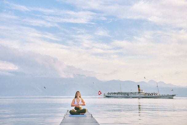 Женевский пейзаж озера, женщина практикует йогу на причале, пароход плавает на заднем плане - Фото, изображение