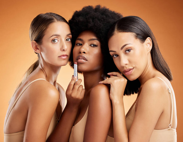 Lipstick, makeup and women with product for beauty against an orange studio background. Face portrait of a model group with facial cosmetics for skincare, body wellness and diversity of people. - Фото, изображение