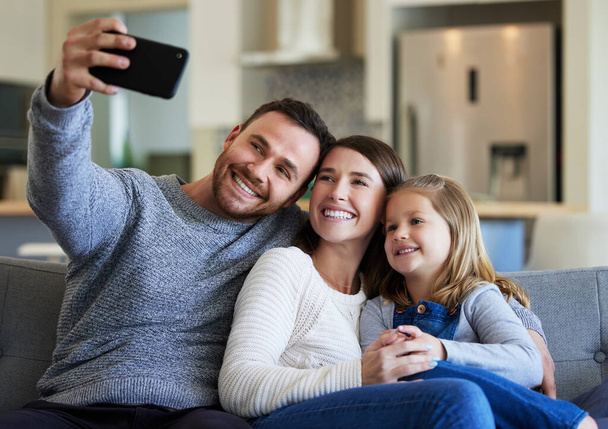 Halten Sie diesen Moment für immer fest. Eine junge Familie macht ein Selfie auf der heimischen Couch - Foto, Bild