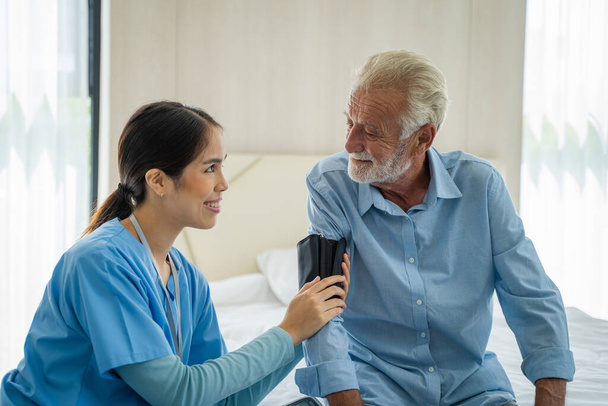 Verpleegster meet bloeddruk aan bejaarde man thuis, concept van de gezondheidszorg, Medisch Consultant. - Foto, afbeelding