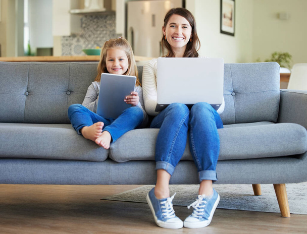Sprawia, że praca w domu jest zabawna. młoda matka i córka korzystające z laptopa i tabletu cyfrowego na kanapie w domu - Zdjęcie, obraz