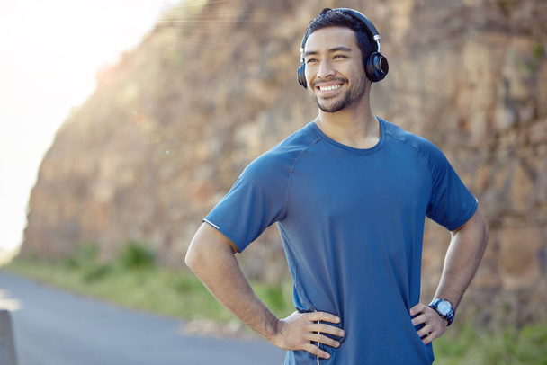 Music helps me workout better. a handsome young man standing alone and listening to music through headphones during his outdoor workout - Photo, Image