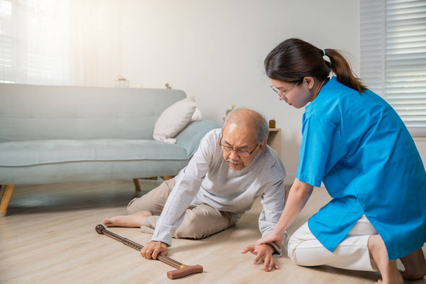 Disabled elderly man patient with walking stick fall on ground and caring assistant at nursing house, Asian senior old man falling down on lying floor and woman nurse helping support in living room - Φωτογραφία, εικόνα
