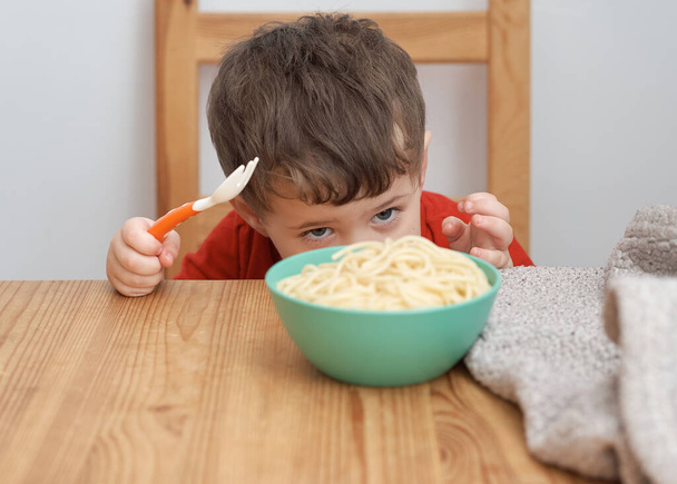 Leuke jongen speelt met zijn pasta tijdens de lunch - Foto, afbeelding
