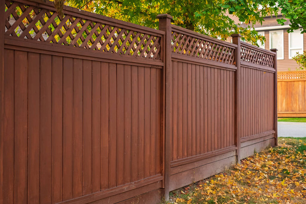 Красивый деревянный забор вокруг дома. Деревянный забор с зеленой лужайкой и осенними листьями. Уличное фото, никого, выборочный фокус - Фото, изображение