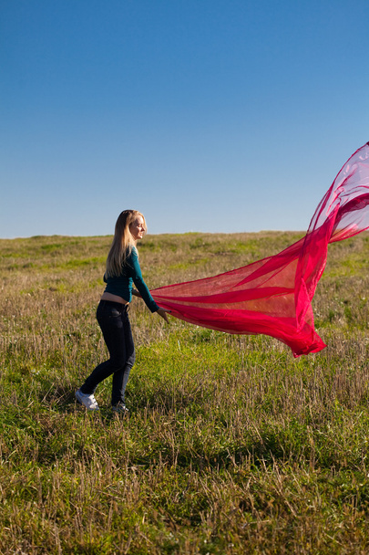 Joven hermosa mujer saltando con tejido en el campo contra
 - Foto, imagen