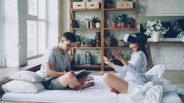 Loving couple is enjoying augmented reality glasses woman is wearing them moving arms and body while her husband is usign tablet touching screen and looking at his excited wife. - Foto, Bild