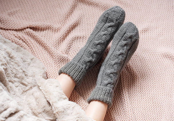 Legs of a young girl in cozy knitted socks. Female legs in warm socks on plaid. Concept of heating season - Photo, Image