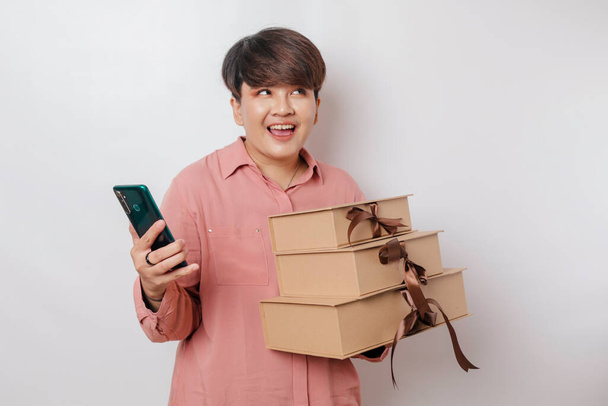 A happy young woman is wearing a pink shirt while holding a stack of presents and her smartphone - Foto, imagen