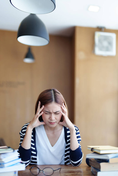 Een portret van een Aziatisch tienermeisje met hoofdpijn en ontmoediging om in de bibliotheek te studeren. - Foto, afbeelding