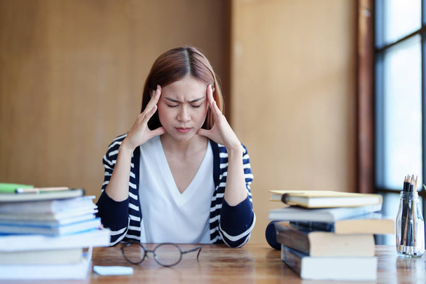 Ritratto di un'adolescente asiatica che mostra mal di testa e scoraggiamento dallo studiare in biblioteca. - Foto, immagini