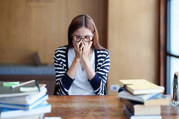 Egy ázsiai tinédzser lány portréja, aki fejfájást és elbátortalanodást mutat a könyvtárban való tanulástól.. - Fotó, kép