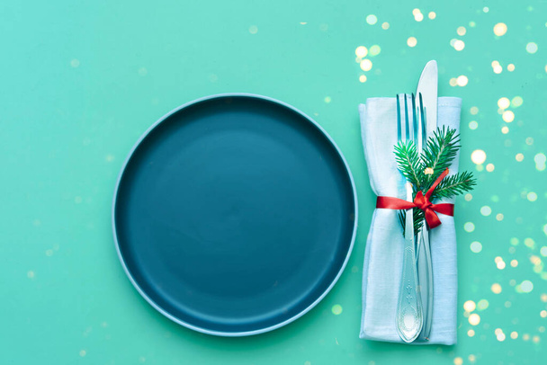 Столовые приборы и ресторанная салфетка на зеленом фоне с блестками. Рождественский или новогодний дизайн для праздника.  - Фото, изображение