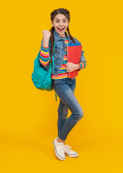 Excited girl making winning gesture. Teen girl back to school. Teenage girl holding books yellow background. School education. - Zdjęcie, obraz
