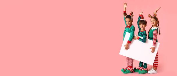 Malé děti oblečené jako elfové držící prázdný plakát na růžovém pozadí s prostorem pro text - Fotografie, Obrázek