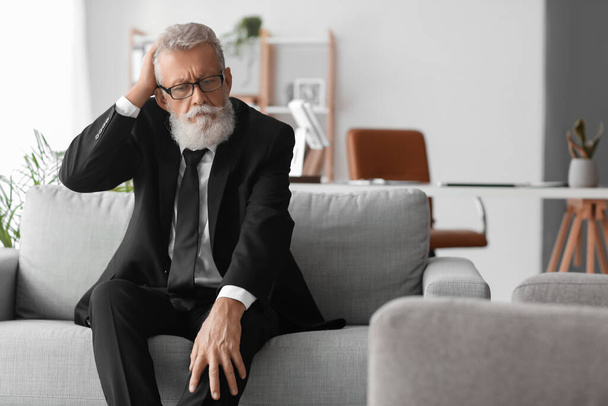 Thoughtful mature man sitting on sofa in office - Foto, Bild