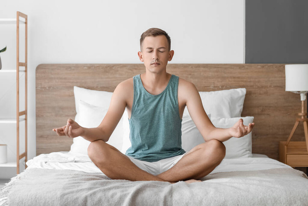 Young man meditating on bed at home - Photo, Image