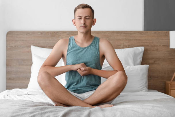 Young man meditating on bed at home - Фото, изображение