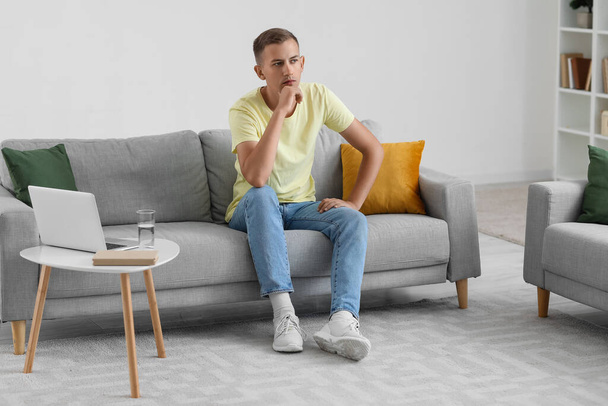 Nachdenklicher junger Mann sitzt zu Hause auf Sofa - Foto, Bild
