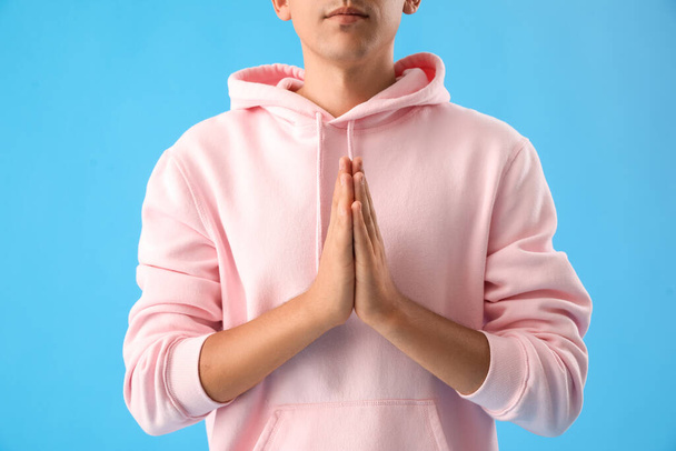 Young man in pink hoodie meditating on blue background, closeup - Photo, Image