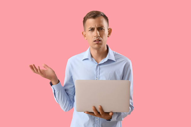 Confuso giovane uomo con computer portatile su sfondo rosa - Foto, immagini