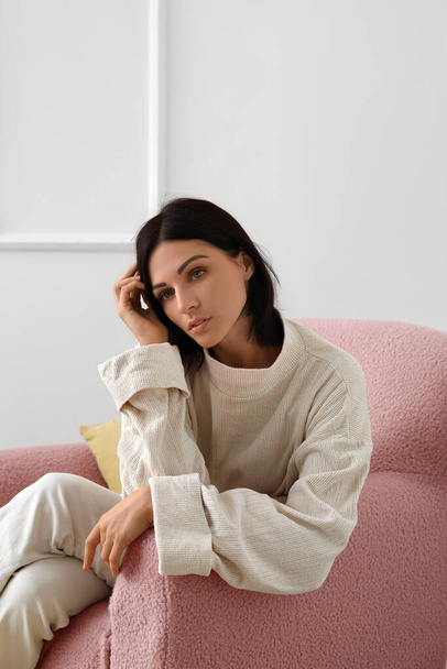 Young woman sitting in beige armchair near light wall - Фото, изображение