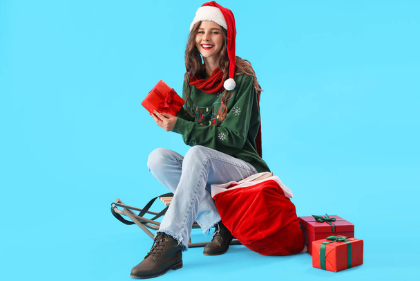 美しい女性でサンタ帽子でバッグとクリスマスプレゼント上の青の背景 - 写真・画像