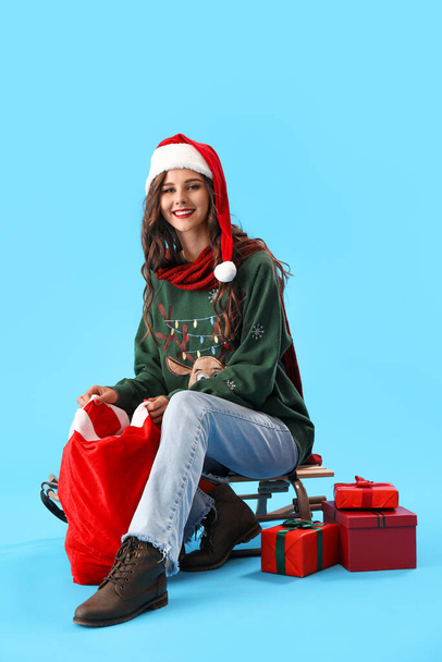 Bella donna in cappello Babbo Natale con borsa e regali di Natale su sfondo blu - Foto, immagini