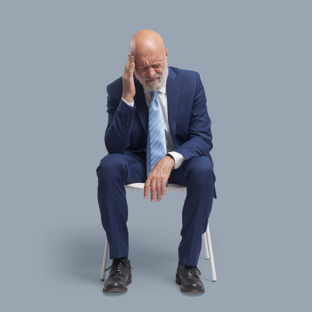 Senior man sitting on a chair, he is having a bad headache - Fotografie, Obrázek