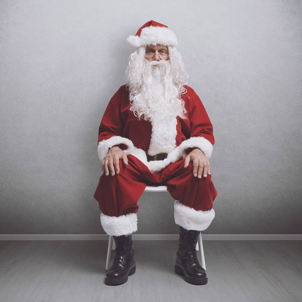 Bored Santa Claus sitting on a chair and waiting for a job interview - 写真・画像