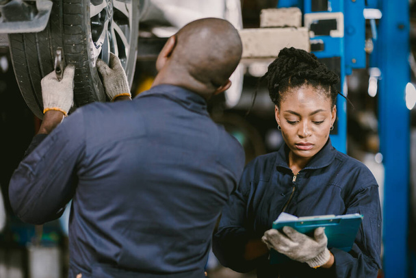 Travailleur d'équipe mécanicien noir africain travaillant ensemble pour réparer réparer pneu de voiture de contrôle ensemble dans le garage - Photo, image