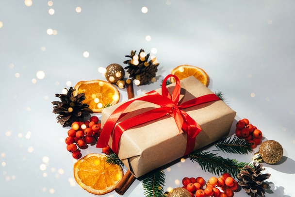 Ein Geschenk, in braunes Papier gewickelt und mit einem Tannenzweig, einem goldenen Spielzeug und einem Tannenzapfen gebunden, orange auf weißem Hintergrund. Ansicht von oben - Foto, Bild