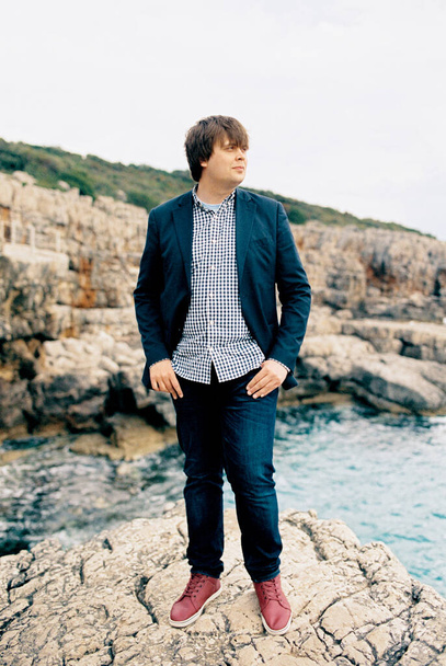 Adam, elleri ceplerinde denizin üzerindeki bir kayanın üzerinde duruyor. Yüksek kalite fotoğraf - Fotoğraf, Görsel