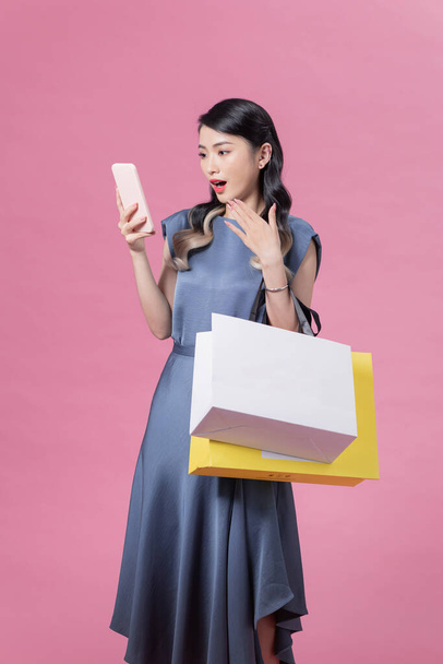 Shocked and excited shopping woman using app on smartphone on pink isolated background - Фото, изображение