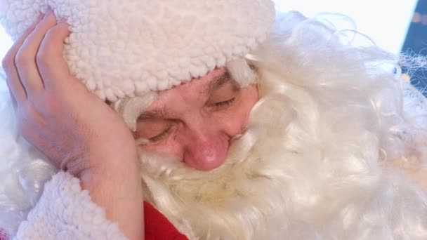彼の腕で寝ているサンタクロースの肖像画がサポートされている。サンタクラスの衣装の面白い男、顔を閉じてください。2023年とクリスマス - 映像、動画