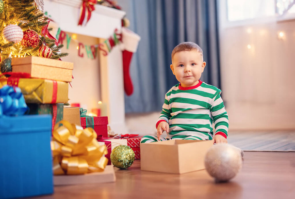 Petit garçon assis sur le sol près du sapin de Noël à l'intérieur. Concept de célébration Noël et Nouvel An en famille. - Photo, image