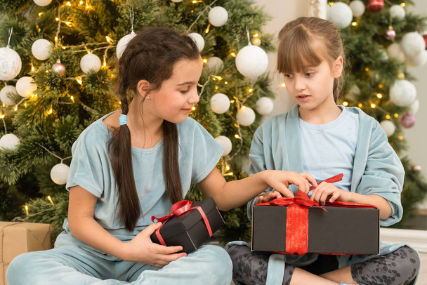 christmas, x-mas, winter, happiness concept - two adorable girls playing near the Christmas tree. - Photo, Image