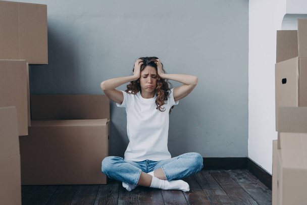 Spanish woman packing cardboard boxes. Homeowner is losing her property. Hopeless young woman in jeans and white t-shirt is sitting on the floor. Problem, bankruptcy and mortgage cheating concept. - Photo, Image