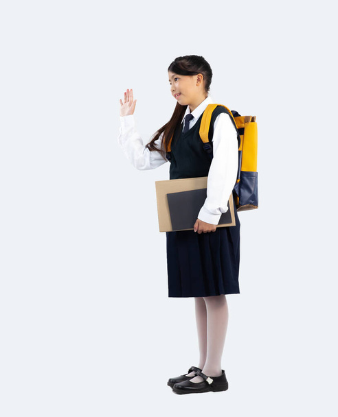 Torniamo al concetto di scuola. Junior scuola ragazza in uniforme studente britannico posa addio su sfondo bianco con piena lunghezza. - Foto, immagini