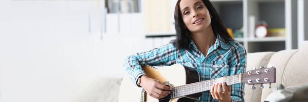 Portrait of pretty brunette woman playing on guitar in living room, female spend free time to learn new hobby on musical instrument. Music, hobby concept - Photo, Image